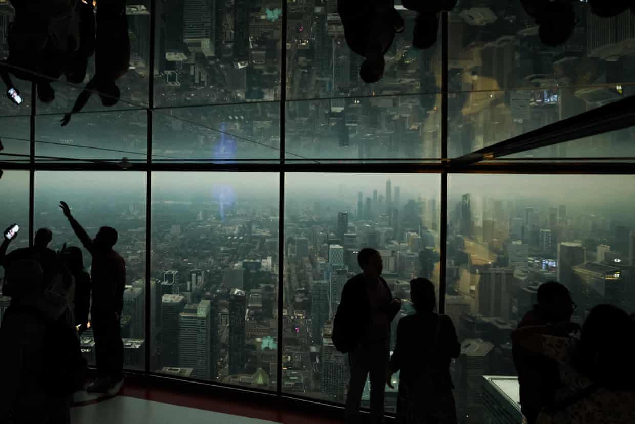 People look out over the city through big glass windows at yellowish-grey haze