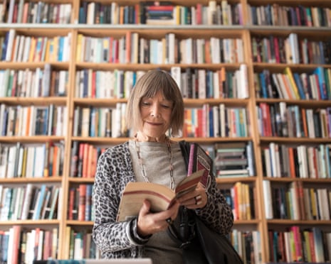Senior woman reading book while standing against fully laden bookshelf
