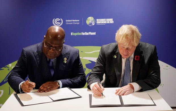 Felix Tshisekedi and Boris Johnson next to each other at a table, each signing papers, at Cop26