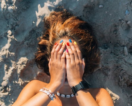 Woman covering face with hands while lying on sand during sunny day