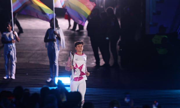 Tom Daley carrying the baton at the Commonwealth Games in Birmingham, accompanied by athletes carrying Pride flags