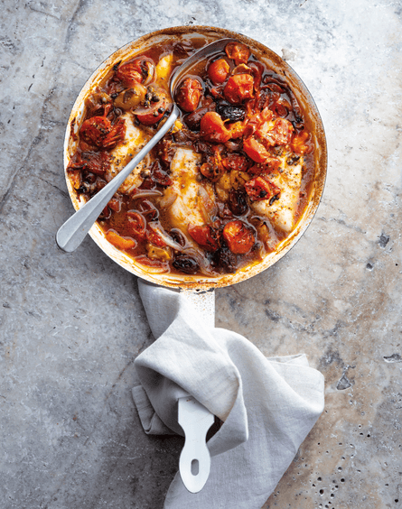 Fish with roasted cherry tomatoes, olives and capers in a serving dish.