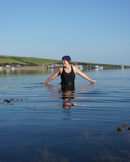 A middle-aged woman, in a swimming costume and cap, wading in a calm sea
