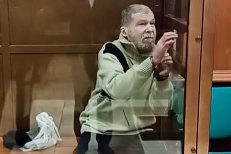 Stephen Hubbard holds his cuffed wrists up while detained behind glass in a Moscow court room during his trial in October 2024