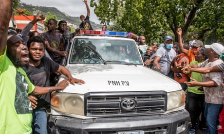 People cheer as a police car drives past at the Petionville Police station where armed men, accused of being involved in the assassination of President Jovenel Moise, are being held in Port au Prince