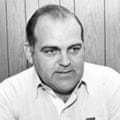 A black-and-white photo showing a balding middle-aged man in a white shirt