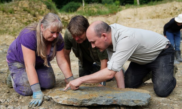 Three people leaning over a chunk of rock