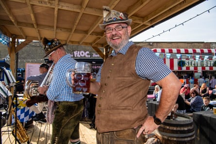 Musicians on stage wearing Bavarian-style hats, one holding a beer and smiling at the camera