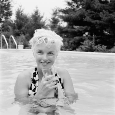 A black and white image of Marilyn Monroe smiling in a swimming pool, holding a glass