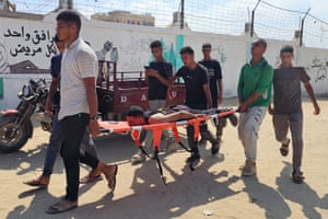 A group of men carry a stretcher with another man lying face down on it past a graffitied wall