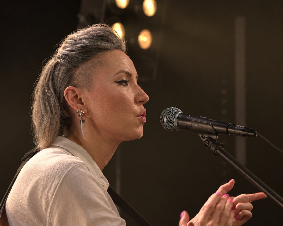 Musician KT Tunstall sings into microphone in dimly lit venue