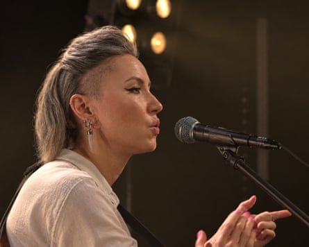 Musician KT Tunstall sings into microphone in dimly lit venue