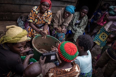Members of the community in Chibuga village listen to the radio as role clay balls and coat them in charcoal to sell as fuel