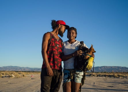 Man in red clothing leans into a woman holding a dog in the desert