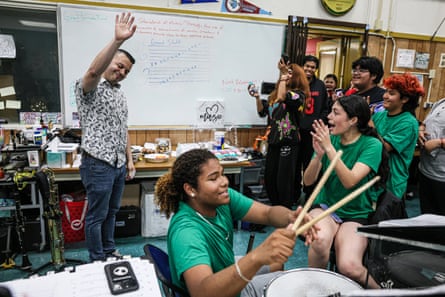 Man waves in classroom as students in green T-shirt applaud and cheer.