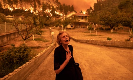 An elderly resident reacts as a wildfire approaches her house in the village of Gouves, on the island of Evia, Greece