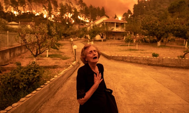 An elderly resident reacts as a wildfire approaches her house in the village of Gouves, on the island of Evia, Greece