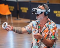 A man wearing a VR headset and a colourful shirt reaches out with controllers, playing a virtual orchestra experience