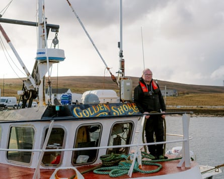 A middle-aged white man standing on the deck of a fishing boat