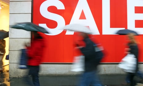 shoppers with brollies pass a sale sign