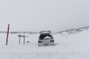 A car is seen snowed in by the side of the road.