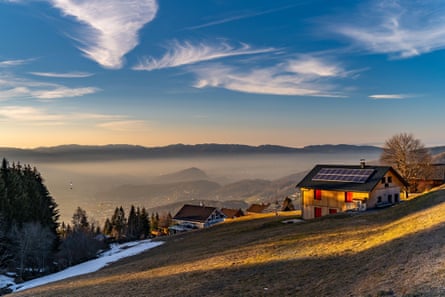 Lodge overlooking a valley in Alps with meadow, mist and some snow