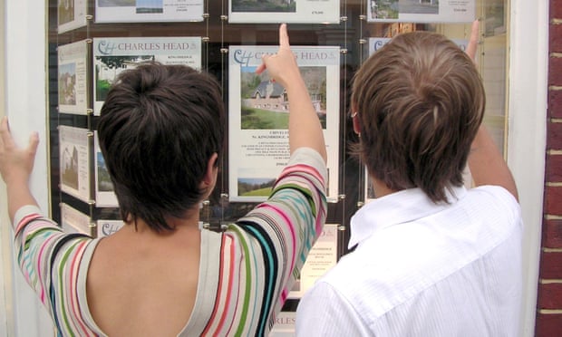 FIRST-TIME BUYERS LOOKING AT PROPERTY IN AN ESTATE AGENTS WINDOW