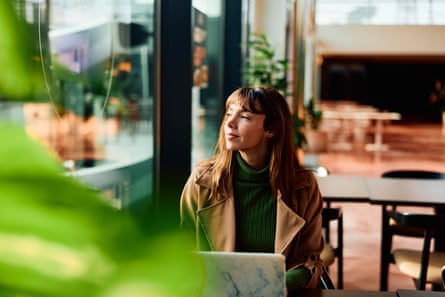 Woman working remotely from cafe looking away pensiveWoman feeling thoughtful and looking through a cafe window while taking a break from working on her laptop, embodying concentration and remote work lifestyle