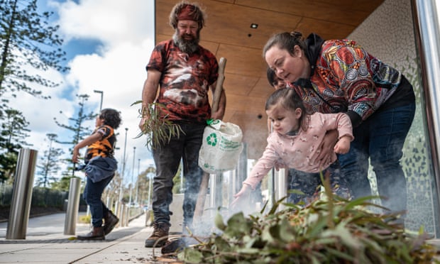 A smoking ceremony is performed by an indigenous man, woman and child outside a building