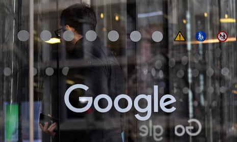 The Google logo can be seen on a glass door as a man passes through the entrance to a building.