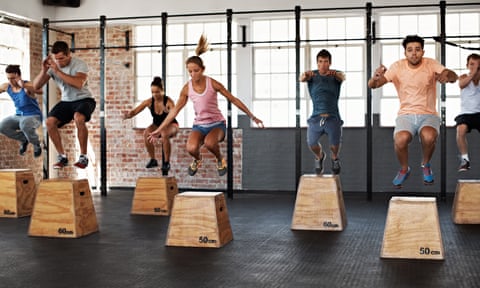 A gym class full of people jumping over high wooden boxes