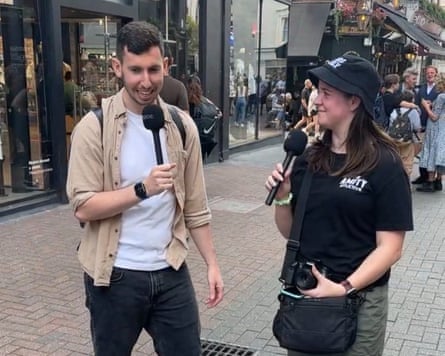 Two people hold microphones while they chat in pedestrianised shopping street