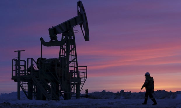 A worker walking past a pump jack on an oil field