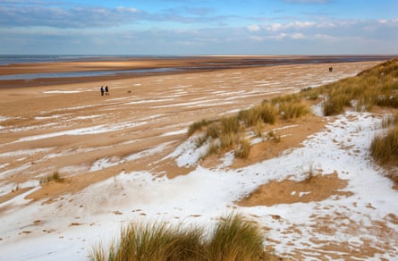 Large beach in winter with dog walkers and a brushing of snow