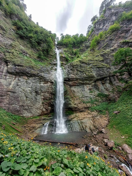 A thin waterfall flows down a rocky cliff face into a pool