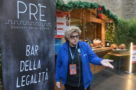 she is middleaged with curly blond hair and glasses, and wears a bright blue fleece; she holds out one hand and looks animated.