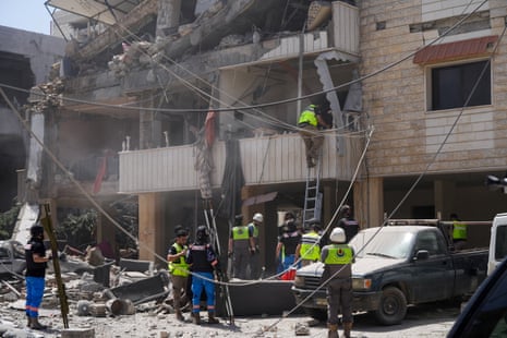 Rescuers in neon high-vis vests and white hard hats climb on ladders up a building that had one side blown out from an Israeli strike. Power lines sag throughout the area.