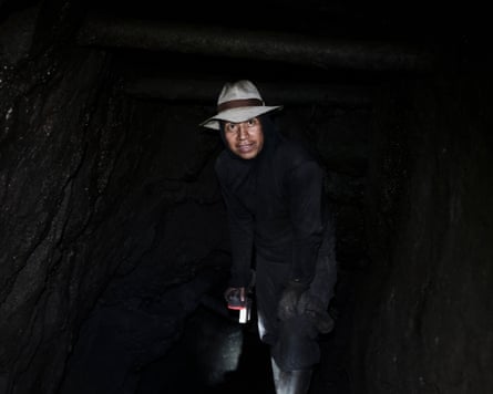 A man’s face is visible in the dark as he looks out of a mine