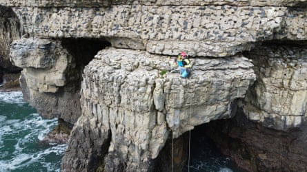 A man uses ropes to install a camera on a cliff ledge above the sea