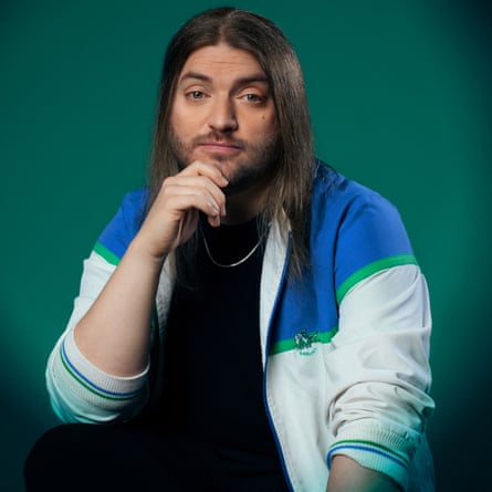 Liam Withnail, in a track top and with a beard and long hair, sits with his elbow on his knee, his hand on his chin, with a quizzical expression