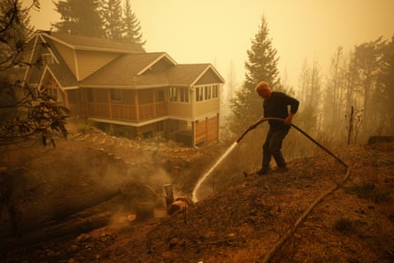 A person puts out a fire hotspot with a house under a hazy sky
