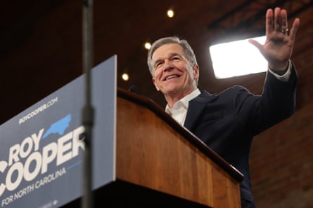A middle-aged man waves from a lectern.