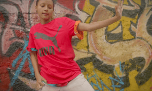 A still from the Suede Gully campaign, showing a girl dancing in front of a spray painted wall