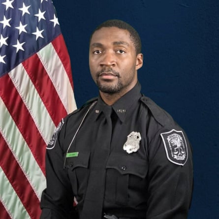 man in police uniform poses in front of american flag