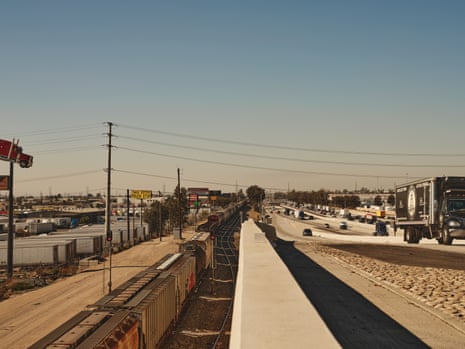 The view from I-10 over Fontana, CA features endless trucks, highway traffic, and a freight train. colors are washed out