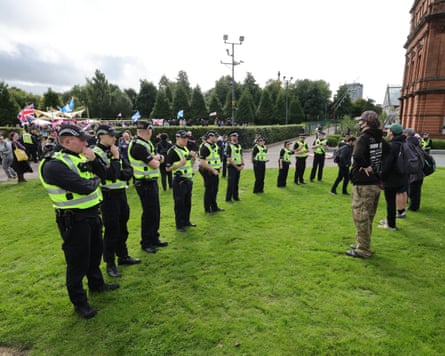 A line of police officers face down a handful of protesters beside the People’s Palace. A crowd waving union jacks and saltires is visible behind the police line