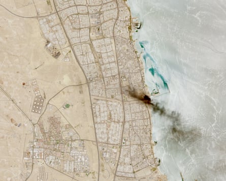 A satellite image shows a plume of smoke stretches from a developed site out to sea