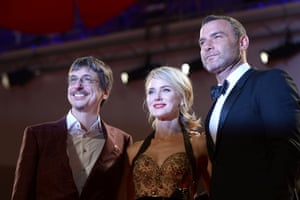 A man in a tuxedo, another man in a brown suit and a woman in an evening gown pose together on the red carpet