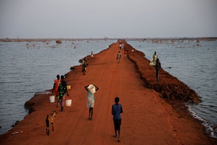 People walk along a dusty red causeway which crosses flood water in South Sudan.