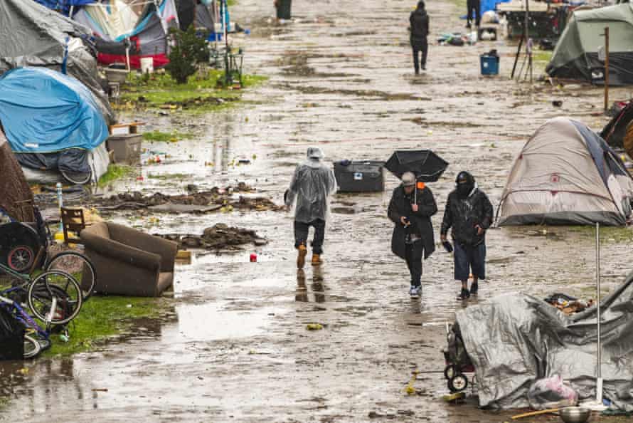 People walk among the tents in the muddy and partially flooded encampment.